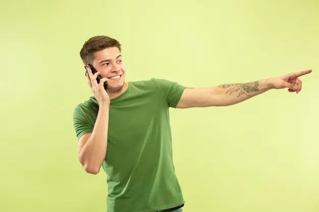 caucasian-young-man-s-half-length-portrait-green-studio-background-beautiful-male-model-shirt-concept-human-emotions-facial-expression-sales-ad-talking-phone-pointing-smiling_155003-25432.webp