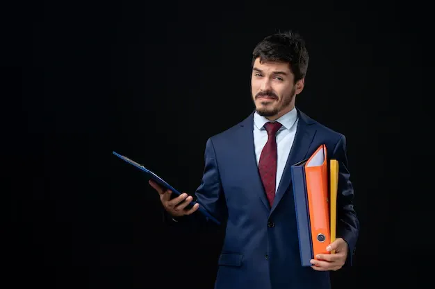 confident-young-adult-suit-holding-several-documents-isolated-dark-wall_140725-97008.webp