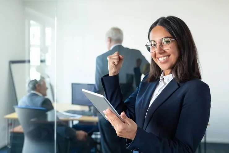 happy-female-professional-glasses-suit-holding-tablet-making-winner-gesture-while-two-businessmen-working-glass-wall-copy-space-communication-concept_74855-14248.webp