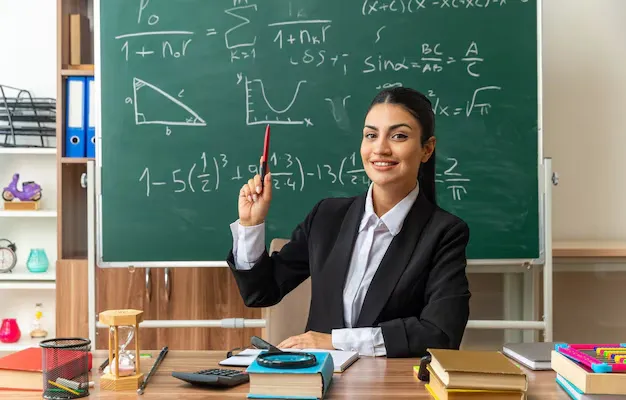 impressed-young-female-teacher-sits-table-with-school-tools-raising-pen-classroom_141793-106366 (1).webp
