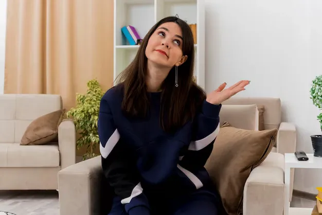 impressed-young-pretty-caucasian-woman-sitting-armchair-designed-living-room-looking-side-showing-empty-hand_141793-57678.webp