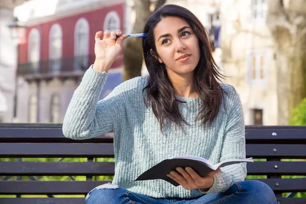 pensive-woman-scratching-head-with-pen-sitting-bench_1262-18988.webp