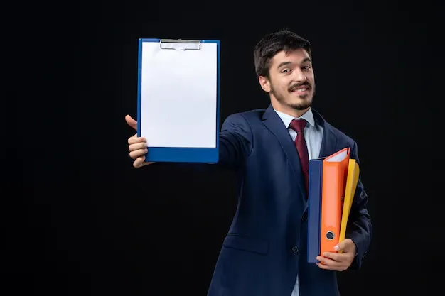 smiling-adult-suit-holding-several-documents-showing-one-them-isolated-dark-wall_140725-96998.webp