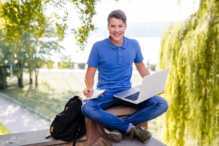 smiling-boy-studying-with-laptop-park_23-2147668957.webp