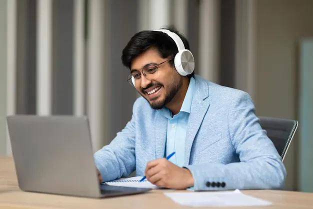 smiling-businessman-wearing-headphones-while-using-laptop-taking-notes_922936-33584.webp