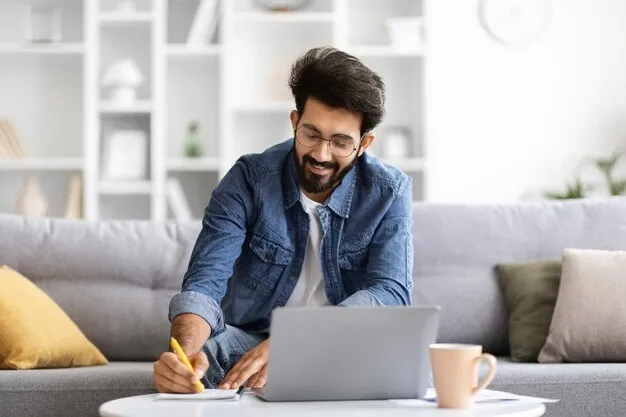 smiling-indian-man-wearing-glasses-writing-notes-beside-laptop-home_116547-97207.webp