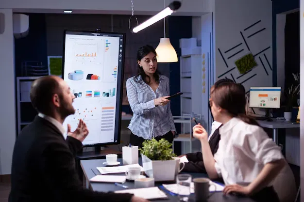 workaholic-businesswoman-pointing-financial-strategy-using-monitor-working-overtime-company-meeting-office-room_482257-2175.webp